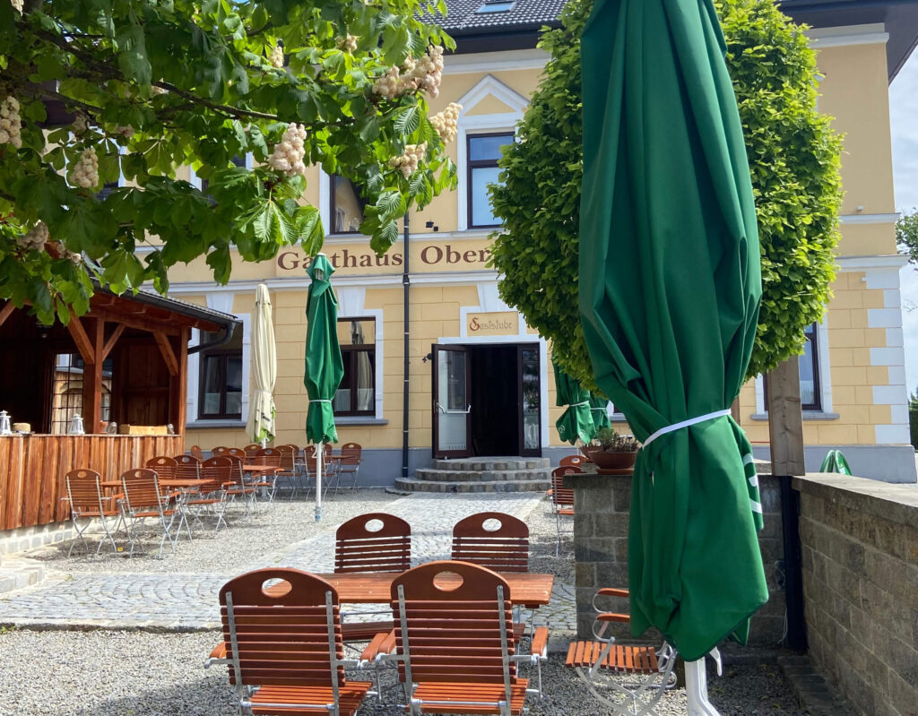 Auf dem Bild sieht man den Oberwirt Lambrechten. Hier werden täglich Ronis Schmankerl von Michelle Siegesleitner gekocht. Man sieht auf dem Bild den Gastgarten des Oberwirt. Auch hier bekommst du typische Österreichisches Essen in der Nähe.